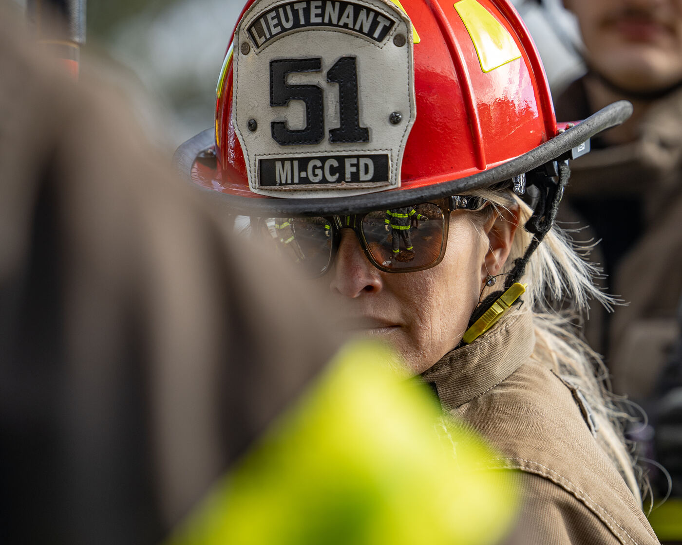 A wildland firefighter carrying a chainsaw against a smoke filled sky